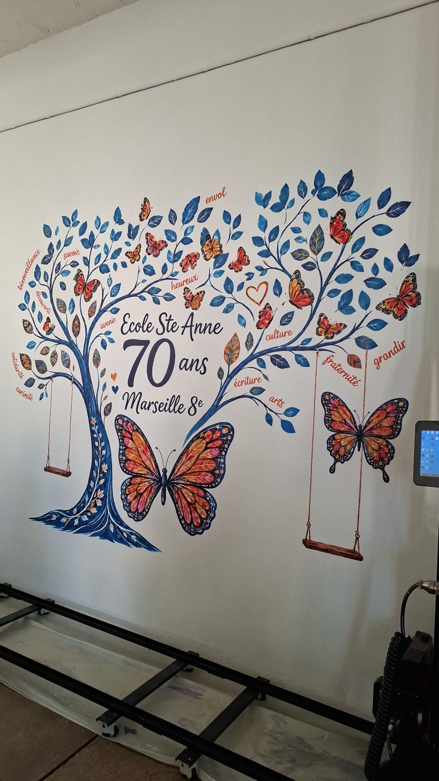 Détail de la fresque murale de l'école Sainte-Anne à Marseille : arbre, papillons, balançoires et mots des valeurs de l'école